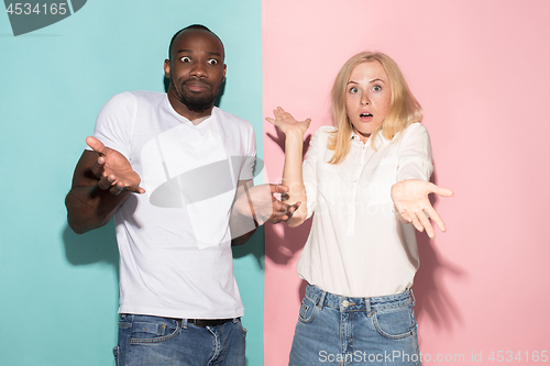 Image of Closeup portrait of young couple, man, woman. One being excited happy smiling, other serious, concerned, unhappy on pink and blue background. Emotion contrasts