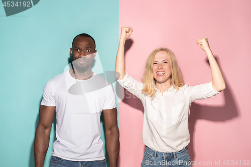 Image of We won. Winning success happy afro man and woman celebrating being a winner. Dynamic image of caucasian female and male model on pink studio.