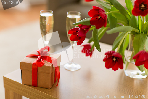 Image of gift box, champagne glasses and flowers on table
