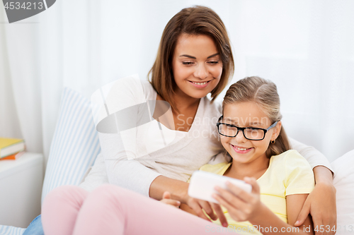 Image of happy mother and daughter with smartphone at home