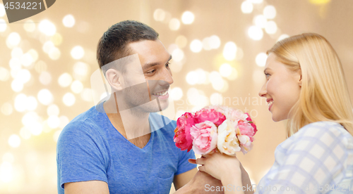 Image of man giving woman flowers over festive lights