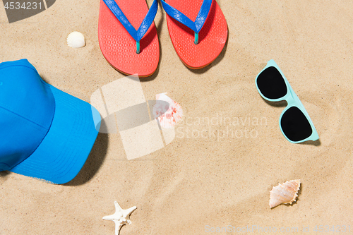 Image of cap, flip flops, shades and on shells beach sand