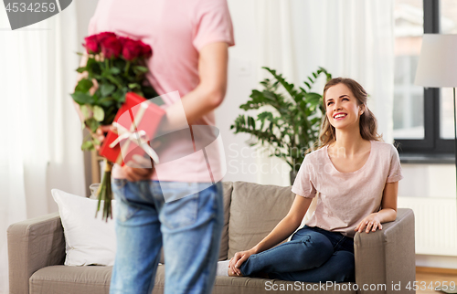 Image of woman looking at man with flowers and gift at home