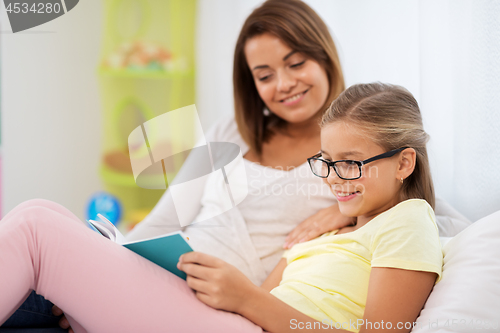 Image of happy girl with mother reading book at home