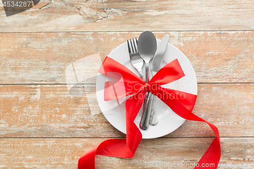 Image of cutlery tied with red ribbon on set of plates