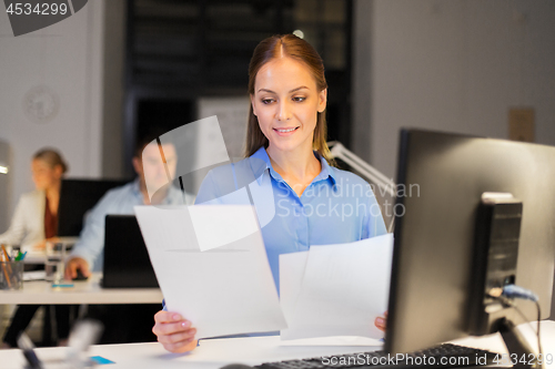 Image of businesswoman with papers working at night office