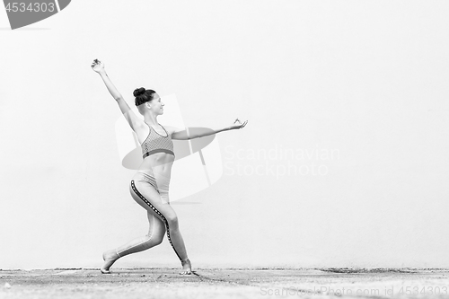 Image of Fit sporty active girl in fashion sportswear doing yoga fitness exercise in front of gray wall, outdoor sports, urban style. Black and white photo.