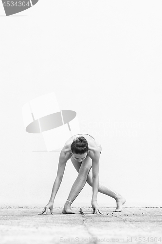 Image of Fit sporty active girl in fashion sportswear doing yoga fitness exercise in front of gray wall, outdoor sports, urban style. Black and white photo.