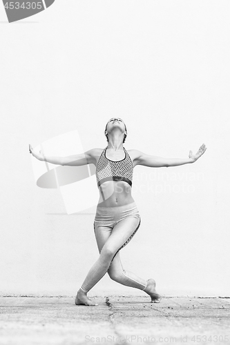 Image of Fit sporty active girl in fashion sportswear doing yoga fitness exercise in front of gray wall, outdoor sports, urban style. Black and white photo.