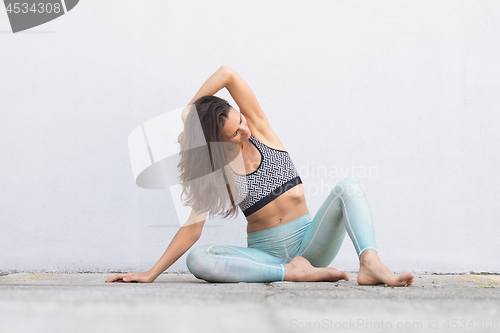 Image of Fit sporty active girl in fashion sportswear sitting on the floor in front of gray wall.