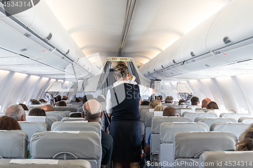 Image of Interior of commercial airplane with stewardess serving passengers on seats during flight.