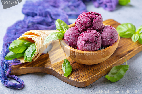 Image of Blueberry ice cream balls and green basil in a wooden bowl.