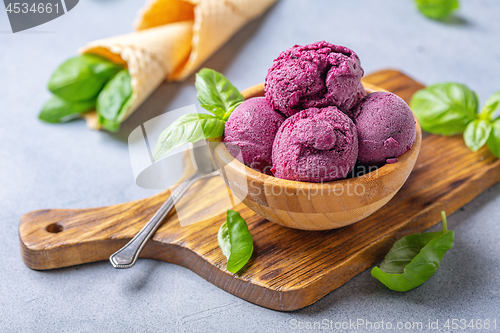 Image of Blueberry ice cream balls and green basil in a wooden bowl.