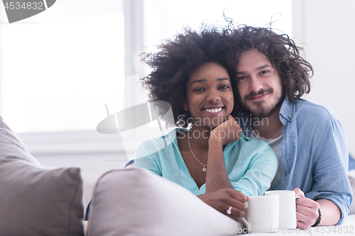 Image of multiethnic couple sitting on sofa at home drinking coffe