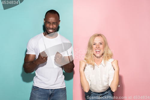 Image of We won. Winning success happy afro man and woman celebrating being a winner. Dynamic image of caucasian female and male model on pink studio.