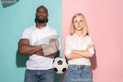 Image of Closeup portrait of young couple, man, woman with football ball. They are serious, concerned on pink and blue background.