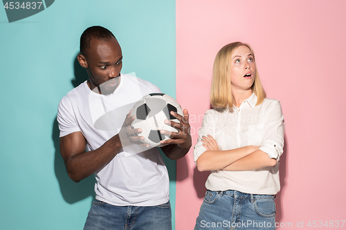 Image of Closeup portrait of young couple, man, woman with football ball. They are serious, concerned on pink and blue background.