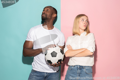 Image of Closeup portrait of young couple, man, woman with football ball. They are serious, concerned on pink and blue background.