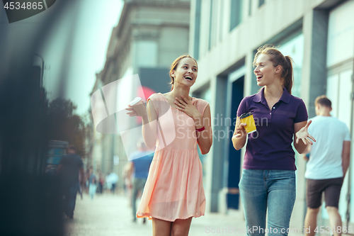 Image of Beautiful girls holding paper coffee cup and enjoying the walk in the city