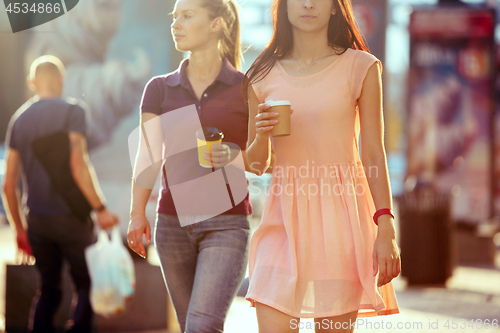 Image of Beautiful girls holding paper coffee cup and enjoying the walk in the city