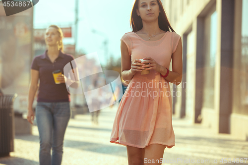Image of Beautiful woman holding paper coffee cup and enjoying the walk in the city