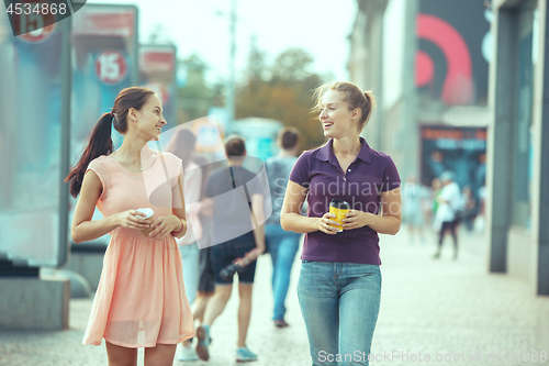 Image of Beautiful girls holding paper coffee cup and enjoying the walk in the city