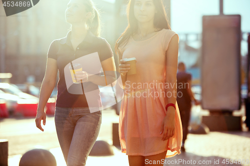 Image of Beautiful girls holding paper coffee cup and enjoying the walk in the city