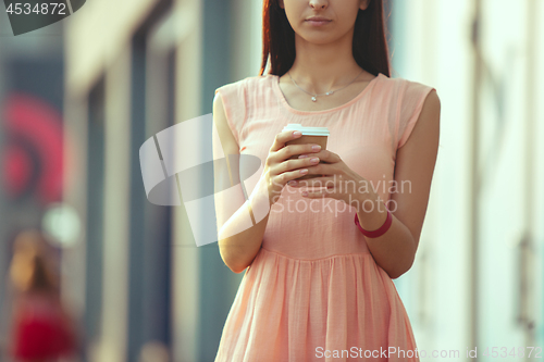 Image of Beautiful woman holding paper coffee cup and enjoying the walk in the city