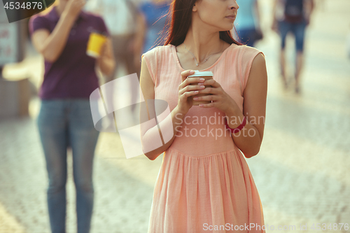 Image of Beautiful woman holding paper coffee cup and enjoying the walk in the city