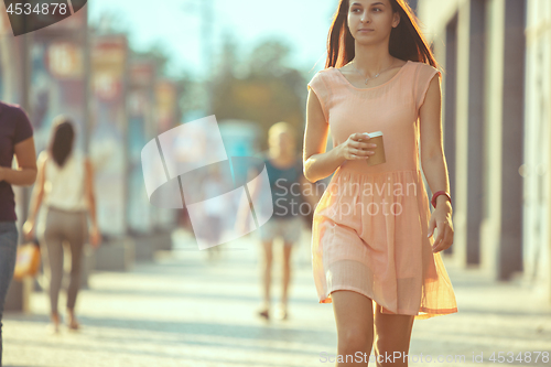 Image of Beautiful woman holding paper coffee cup and enjoying the walk in the city