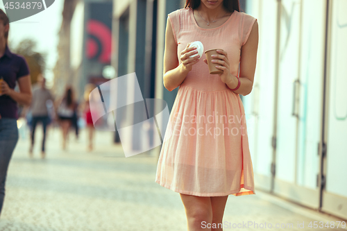 Image of Beautiful woman holding paper coffee cup and enjoying the walk in the city