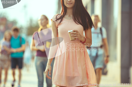 Image of Beautiful woman holding paper coffee cup and enjoying the walk in the city