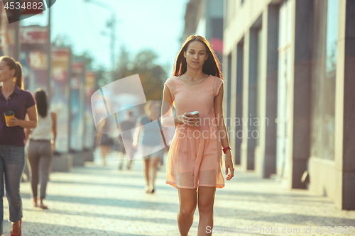 Image of Beautiful woman holding paper coffee cup and enjoying the walk in the city