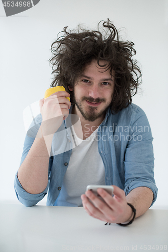 Image of young man eating apple and using a mobile phone  at home