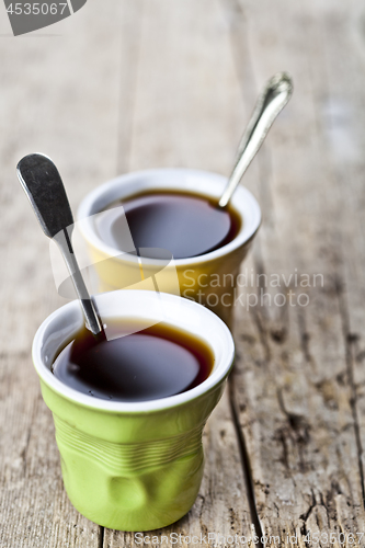 Image of Green and yellow cups with black coffe and spoons on rustic wood