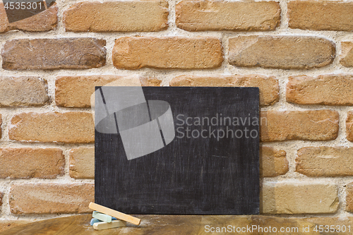 Image of Blank clean blackboard an chalk on wooden table at brick wall. 