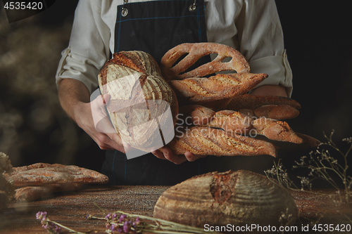 Image of Baker in black apron holds variety of bread