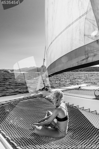 Image of Beautiful woman relaxing on a summer sailing cruise, sitting and sunbathing in hammock of luxury catamaran sailing around Maddalena Archipelago, Sardinia, Italy.