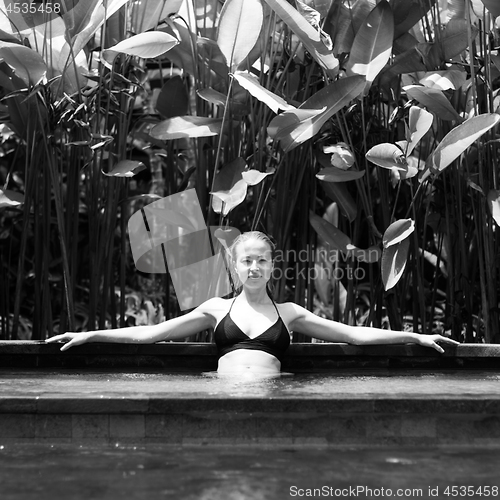 Image of Sensual young woman relaxing in outdoor spa infinity swimming pool surrounded with lush tropical greenery of Ubud, Bali. Black and white image.