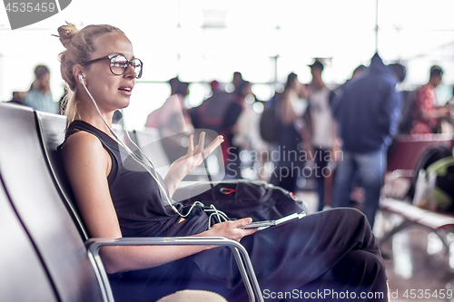 Image of Female traveler talking on cell phone while waiting to board a plane at departure gates at asian airport terminal.