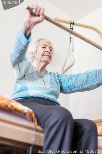 Image of Elderly 96 years old woman exercising with a stick sitting on her bad.