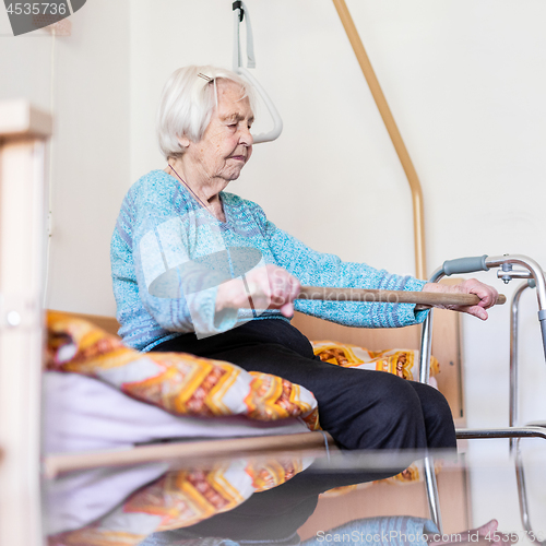 Image of Elderly 96 years old woman exercising with a stick sitting on her bad.