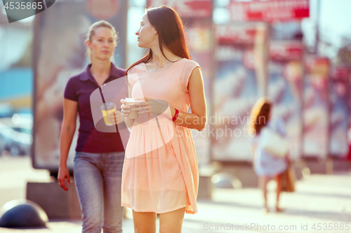 Image of Beautiful girls holding paper coffee cup and enjoying the walk in the city