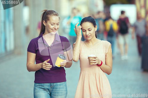 Image of Beautiful girls holding paper coffee cup and enjoying the walk in the city
