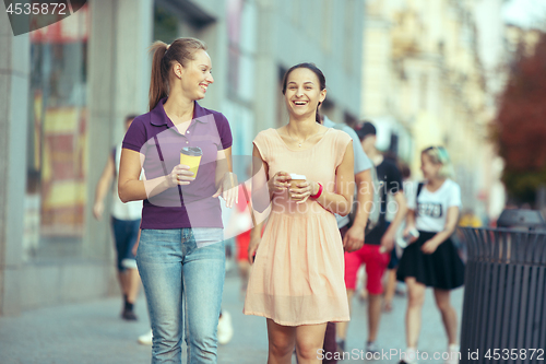 Image of Beautiful girls holding paper coffee cup and enjoying the walk in the city