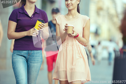 Image of Beautiful girls holding paper coffee cup and enjoying the walk in the city
