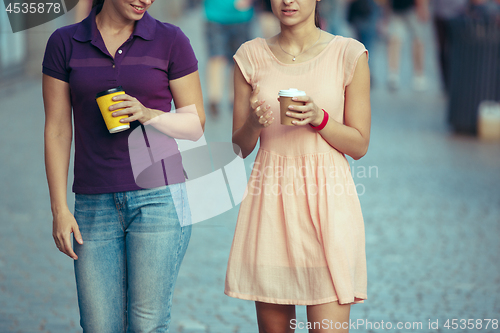 Image of Beautiful girls holding paper coffee cup and enjoying the walk in the city