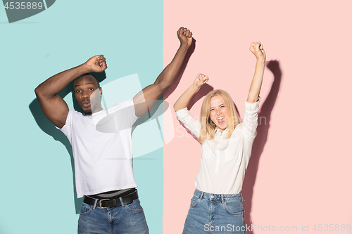 Image of We won. Winning success happy afro man and woman celebrating being a winner. Dynamic image of caucasian female and male model on pink studio.