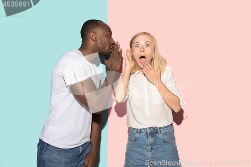 Image of The young couple whispering a secret behind her hand over studio background