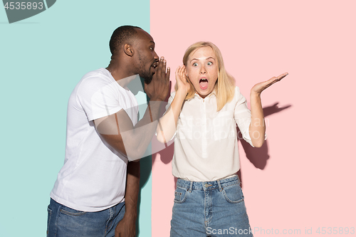 Image of The young couple whispering a secret behind her hand over studio background